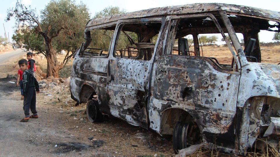 Syrian children walk past a minibus damaged during a US raid near the Syrian village of Barisha (27 October 2019)